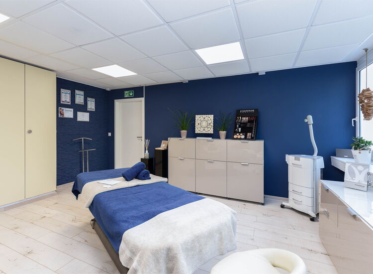 behandlungsraum mit liege, beigen möbeln und blauer wand und medizinischem Gerät